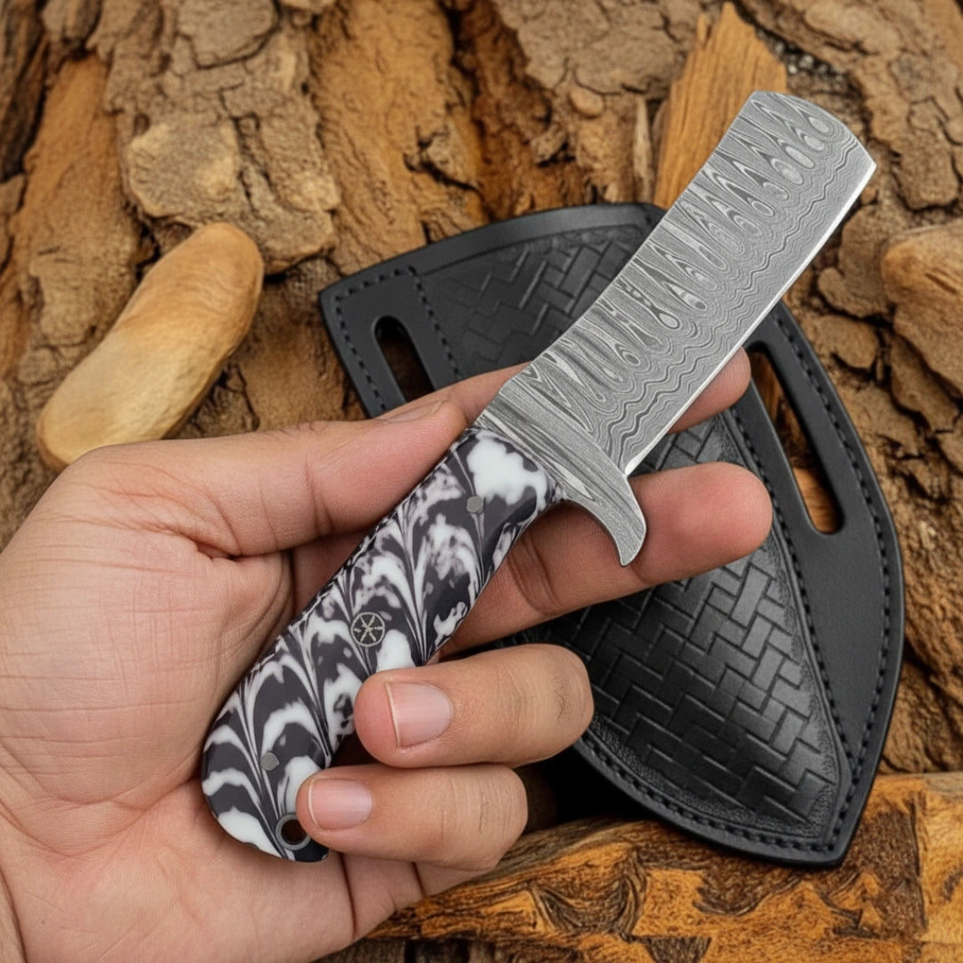 A hand holding an 8-inch handmade Damascus calf cutter knife, featuring the black-and-white resin handle and a sharp, patterned Damascus blade, positioned on a leather sheath.