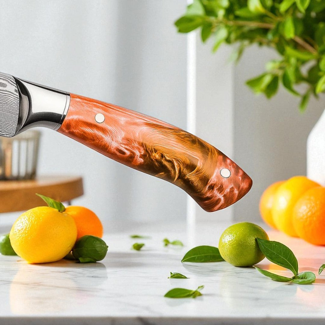  Close-up of the orange and brown swirled resin handle of a Damascus paring knife, with various citrus fruits in the background.
