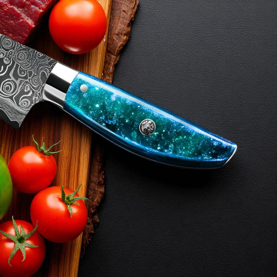 Close-up of the vibrant blue and green "Ocean Sky" resin handle of a Damascus kitchen knife next to red tomatoes.
