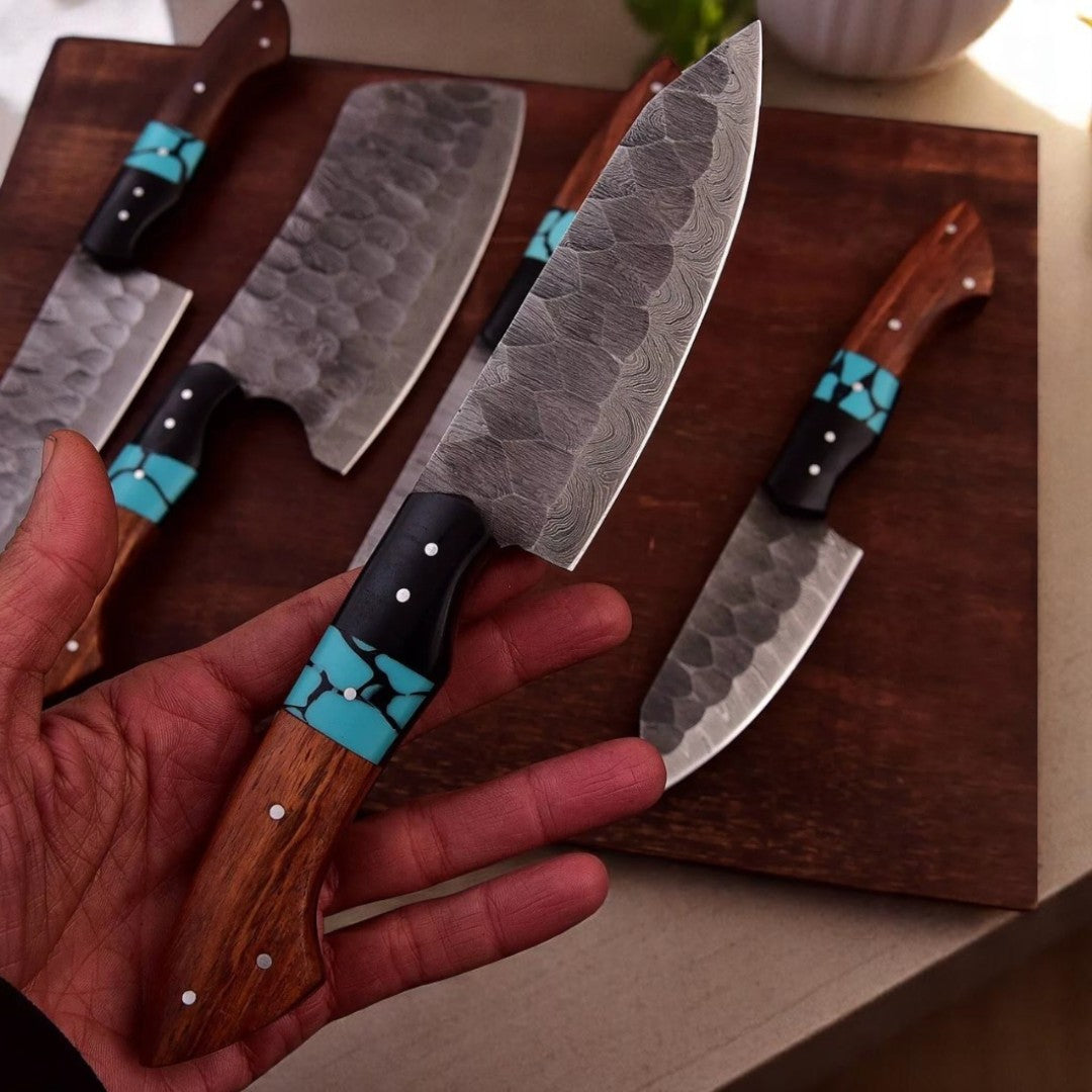 Hand holding a Water Ripple Damascus Chef Knife with wood and turquoise resin handle, part of a 5-piece set, on a wooden cutting board

