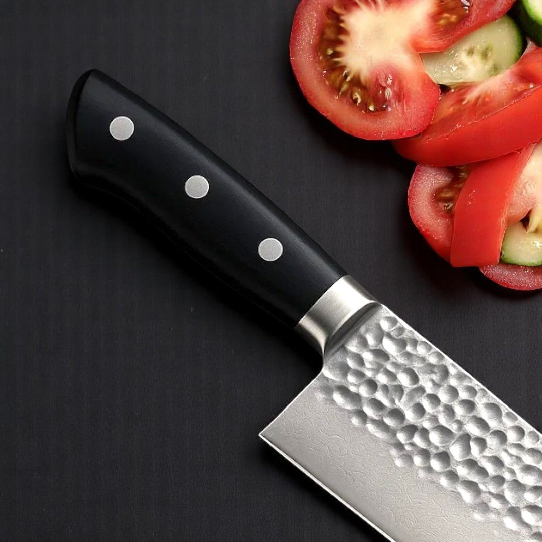 Close-up of Black Resin Handle on Hammered Santoku Knife next to sliced tomatoes and cucumber

