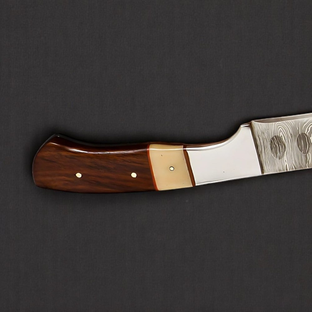 Close-up of Damascus steel brisket knife handle with polished wood grip and brass accent.