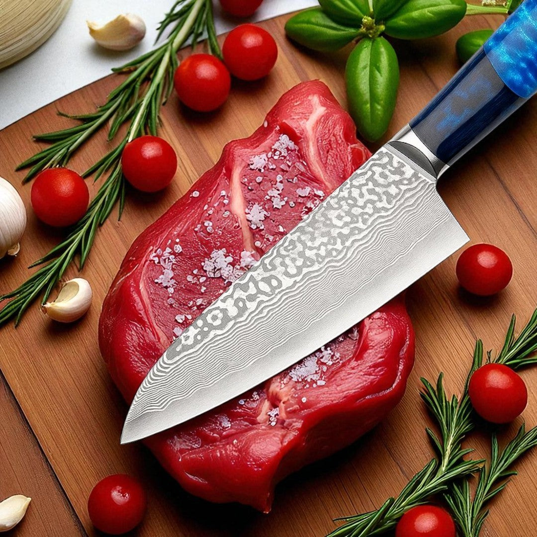 High-quality Damascus steel chef knife slicing raw steak, surrounded by rosemary, cherry tomatoes, garlic, and coarse salt on a wooden cutting board.