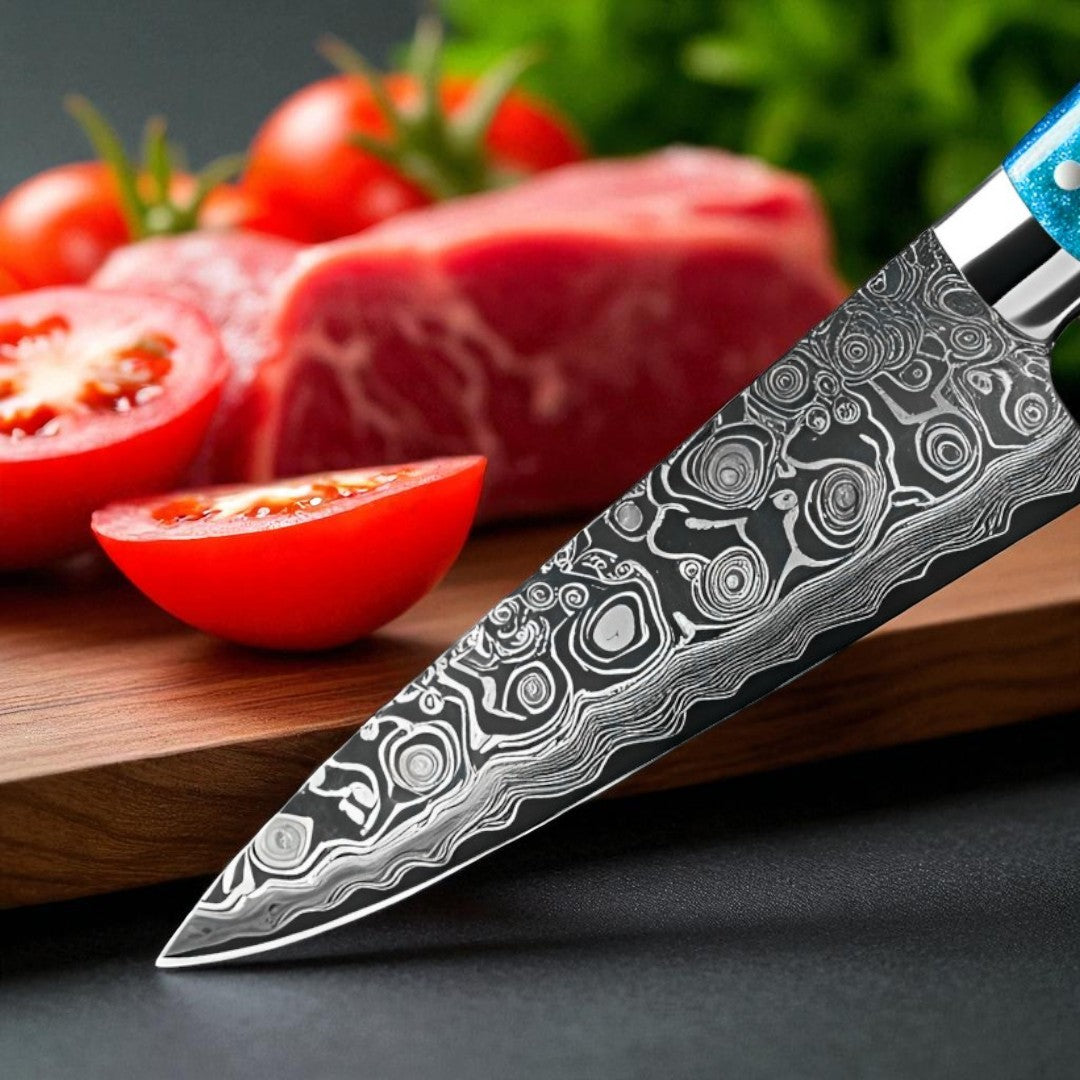 Detailed close-up of the intricate wavy Damascus pattern on the blade of the Ocean-Sky-Series kitchen knife, with raw meat and tomatoes blurred in background.