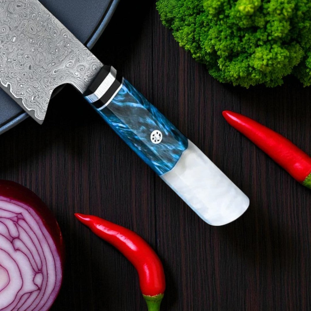 Damascus chef knife with beautiful blue & white resin handle, cutting red onion and chili peppers on a sleek kitchen counter.