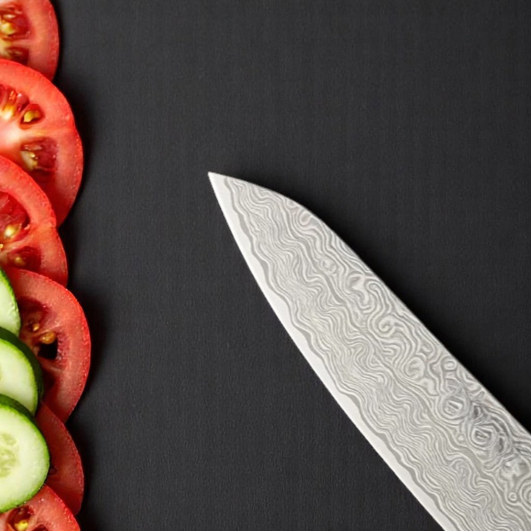 Close-up of Damascus pattern blade tip of a Santoku knife with sliced tomatoes and cucumbers







