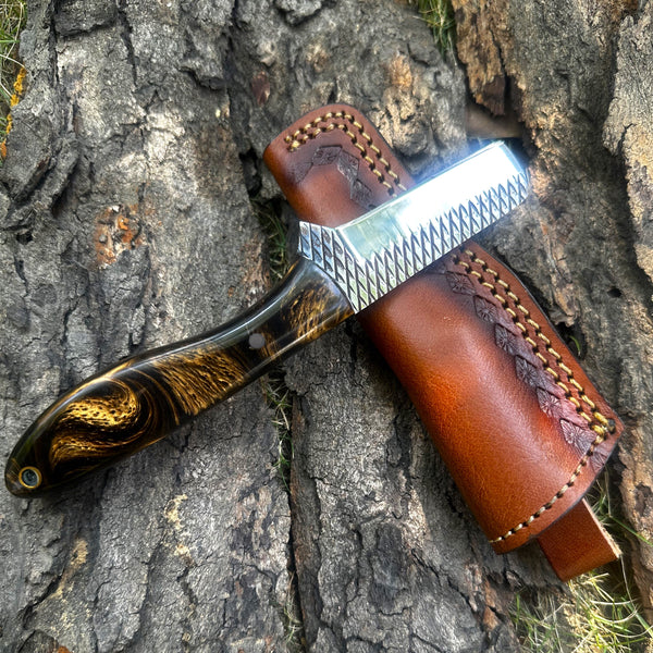 Rasp Steel Bull Cutter Knife with a wooden handle and leather sheath on a textured stone surface
