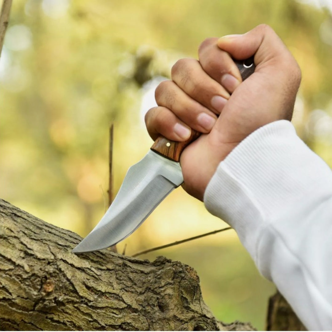 Hand holding a Handmade Cowboy Fixed Blade Knife, with polished blade and two-tone wood handle, testing its edge on a tree branch.

