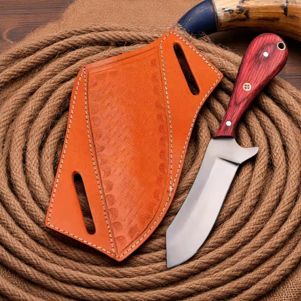Carbon Steel Bull Cutter Knife with red Pakkawood handle and brown leather sheath, resting on a coiled rope on a wooden surface.