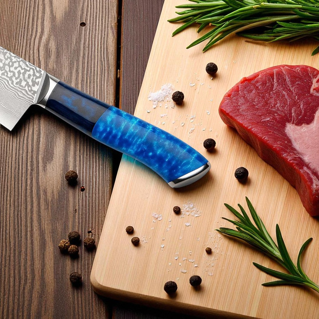 A close-up of a Damascus steel chef knife with a vibrant blue and dark blue patterned resin handle, resting on a light wooden cutting board. Black peppercorns, salt crystals, and fresh rosemary sprigs are scattered around a piece of red meat.