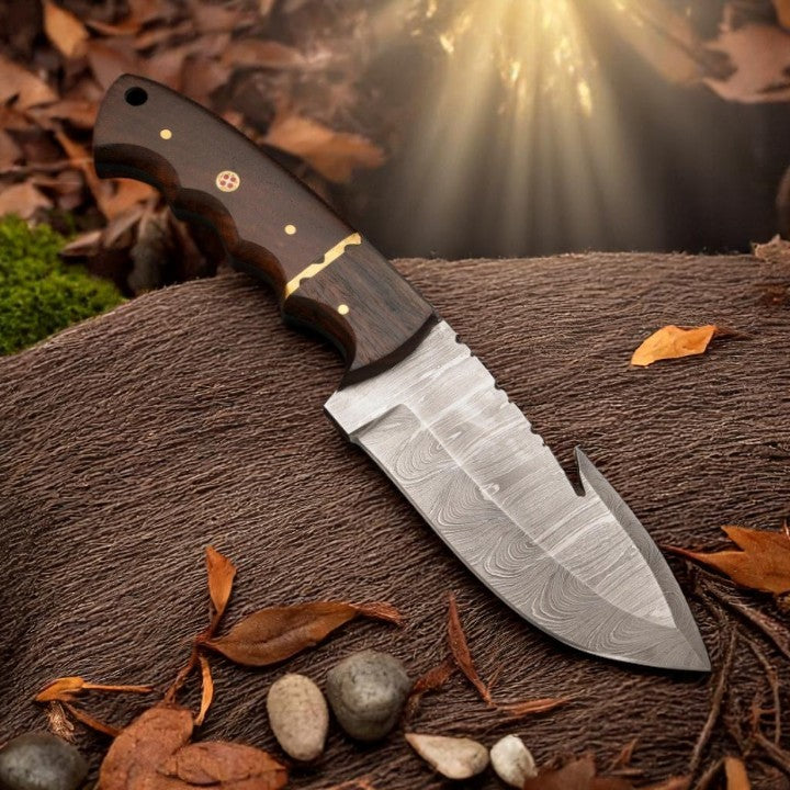 Damascus Gut Hook Skinner Knife with wood handle, held over a deer hide, demonstrating its use for skinning.







