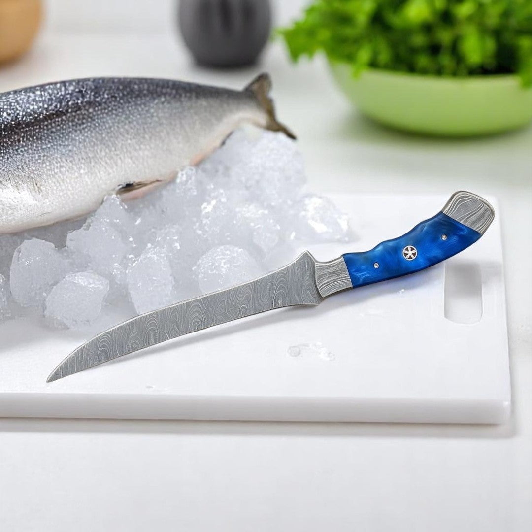 Damascus Fillet Knife with blue swirled resin handle resting on a white cutting board, with a fish on ice and fresh herbs in the background
