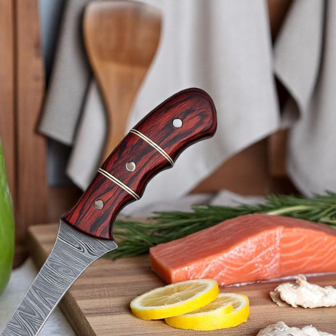 Handmade Damascus Steel Fillet Fishing Knife with Red Pakka Wood handle and brass accents, shown on a wooden cutting board next to a salmon fillet and lemon slices