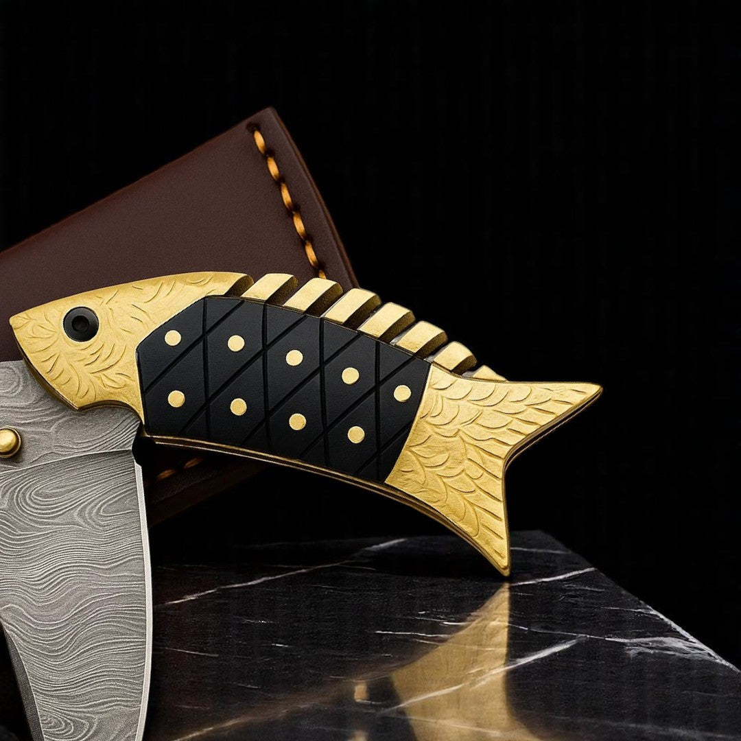Close-up view of the gold-toned fish-shaped handle of a Damascus Folding Knife, showing black textured inlays and decorative gold 