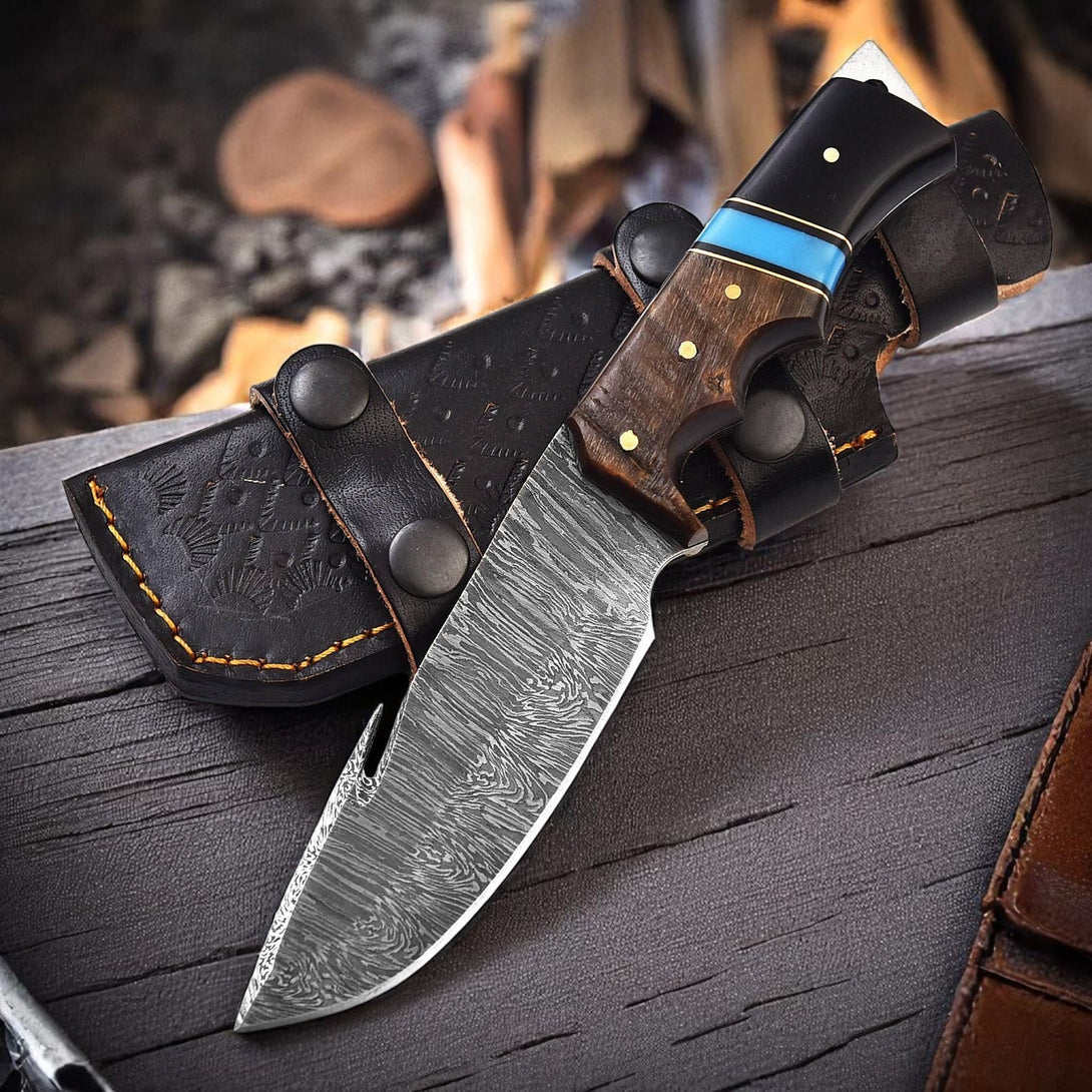 Handmade Damascus Knife with blue, black, and wood handle, resting on a wooden surface with salt and a green container in the background.

