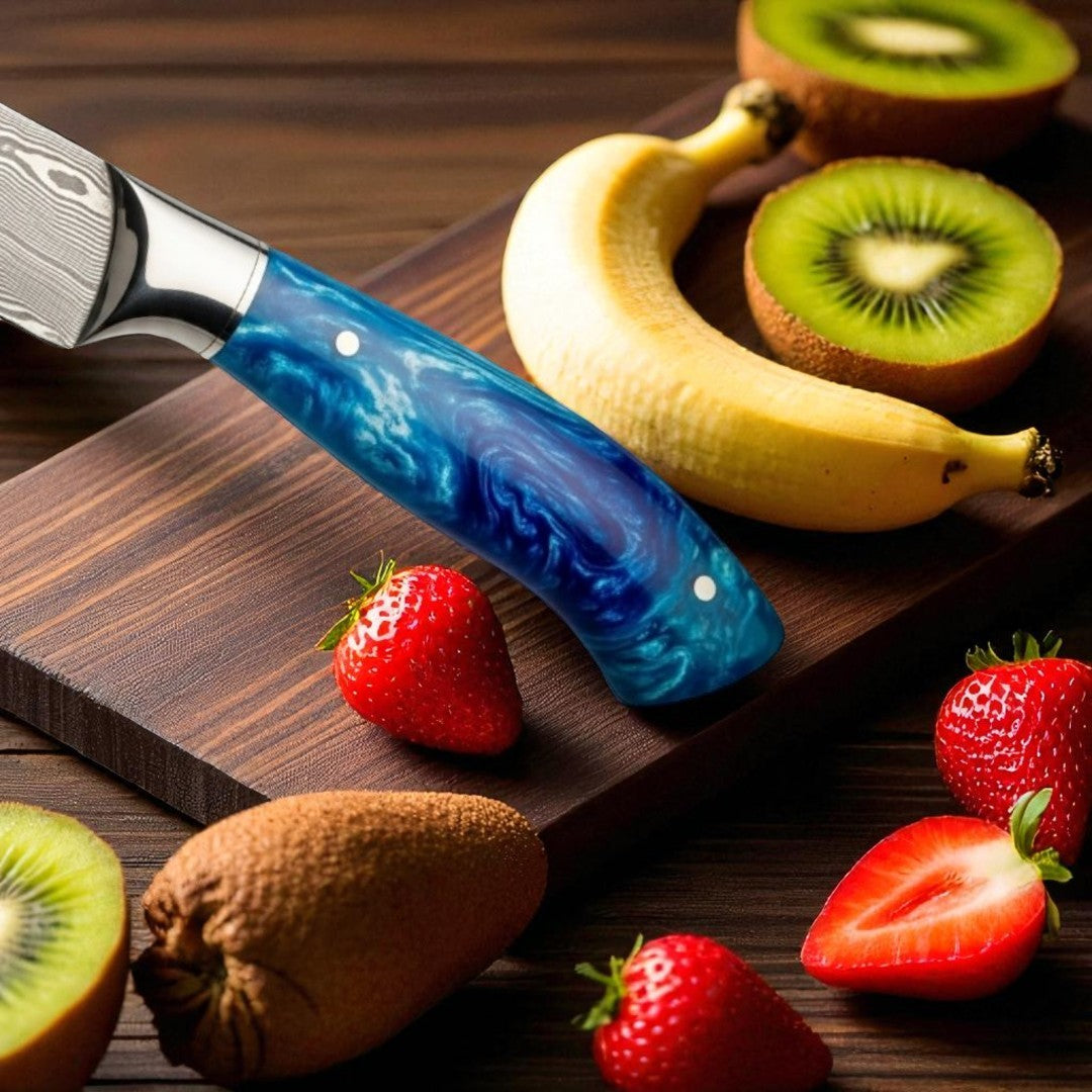 Overhead view of Damascus Paring Knife with blue swirled resin handle, closed, resting on a dark wooden surface next to fresh fruit.