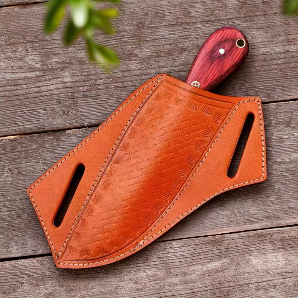 Overhead view of a Carbon Steel Bull Cutter Knife with red Pakkawood handle, displayed next to its brown leather cover on a fur-like background.