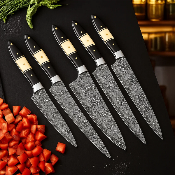 Set of five Damascus knives on a black surface with chopped vegetables.