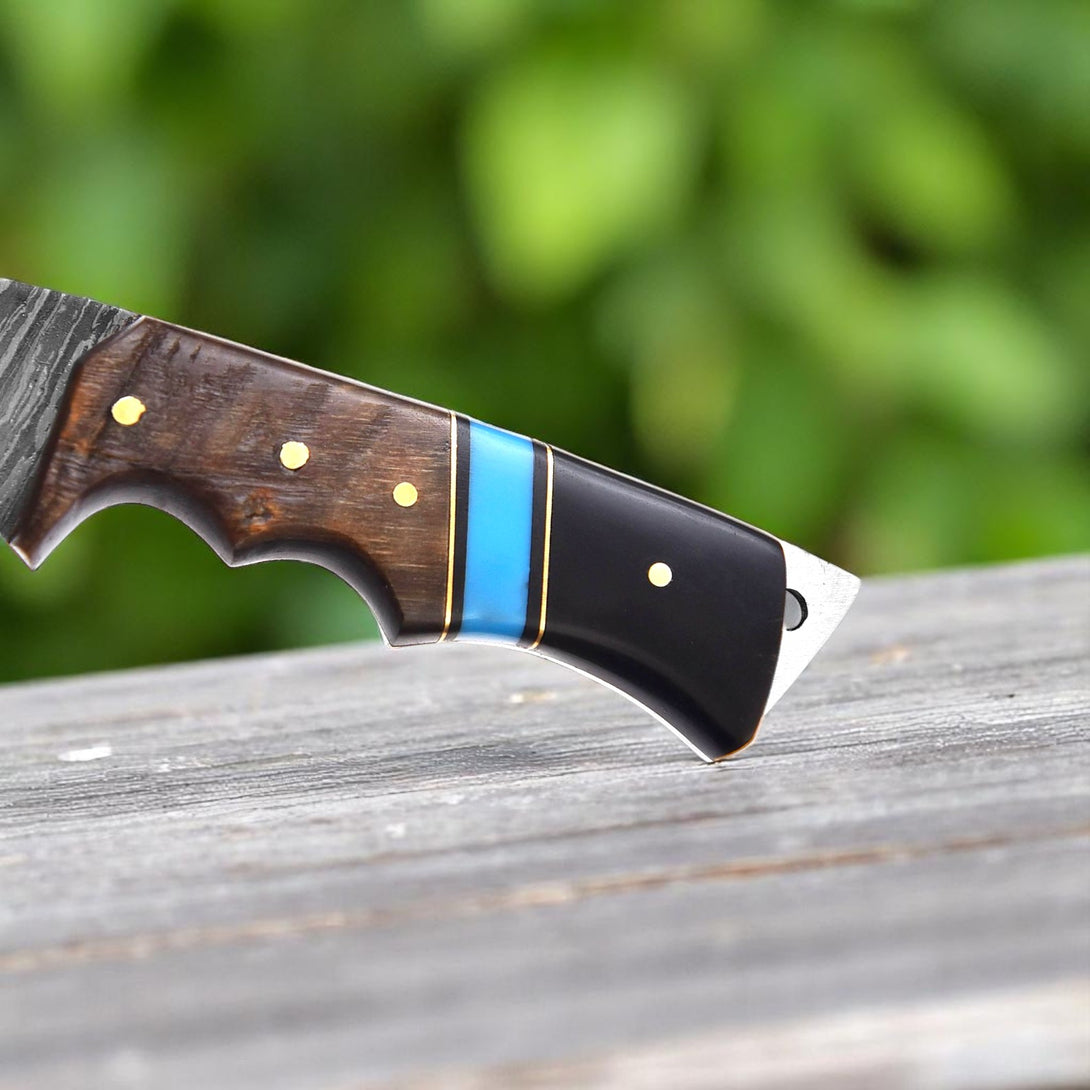 Close-up view of the multi-segment blue, black, and wood handle of a Premium Damascus Hunting Knife, showing its detail and brass accents.

