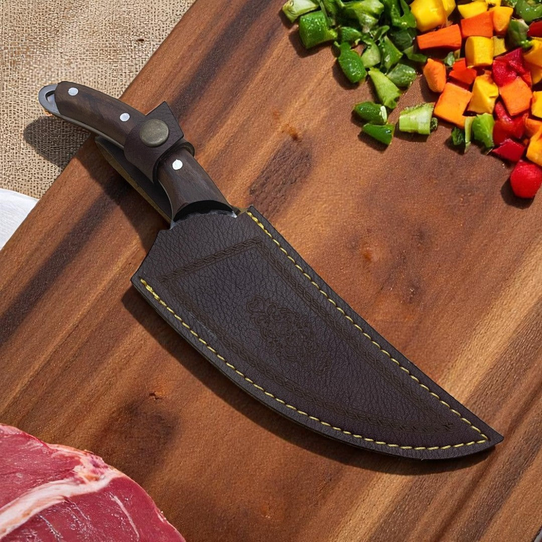 Viking Hand-Foraged Boning Knife with finger hole, resting in its brown leather sheath on a wooden cutting board with fresh ingredients.

