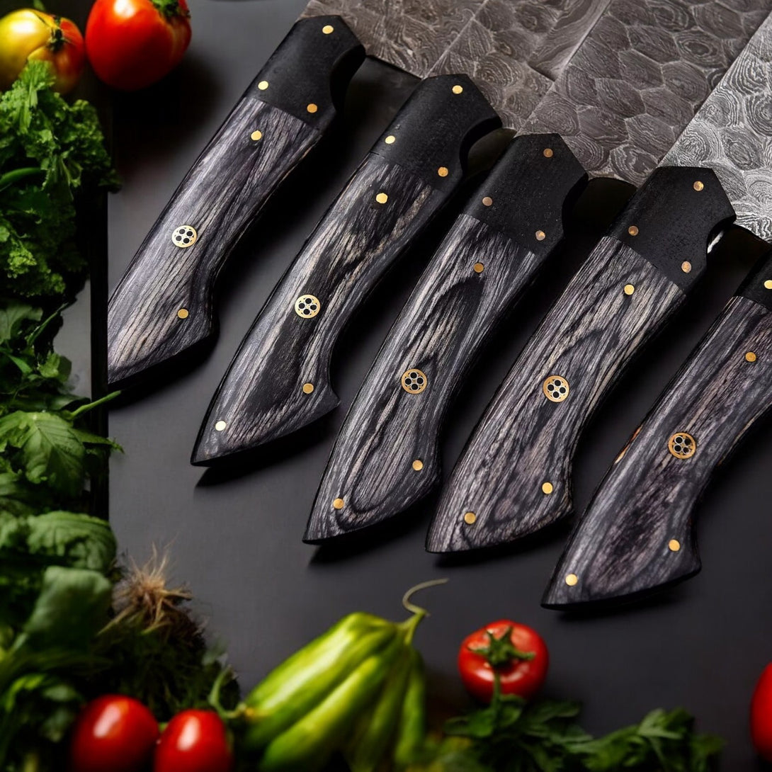 Close-up view of the dark wood handles with brass accents and rivets of five Damascus steel kitchen knives, arranged on a dark surface with vegetables








